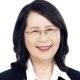 Portrait of Namtip Wipawin, a smiling woman with shoulder-length dark hair and rimless glasses, wearing a black blazer over a white collared shirt against a plain white background.
