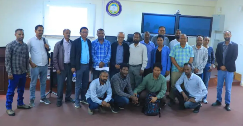 A group photo of about 20 workshop participants in a meeting room, with four people kneeling in the front row.